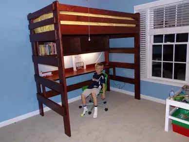 A boy is sitting under a bunk bed with a desk underneath it
