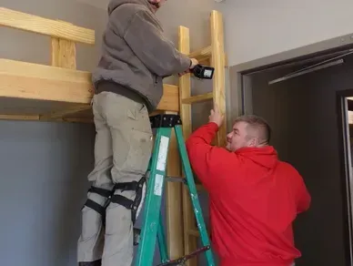 Two men are working on a ladder in a room.