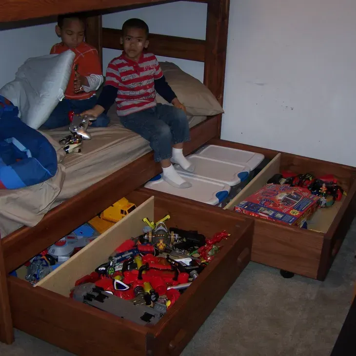 Two boys are sitting on a bunk bed with drawers full of toys