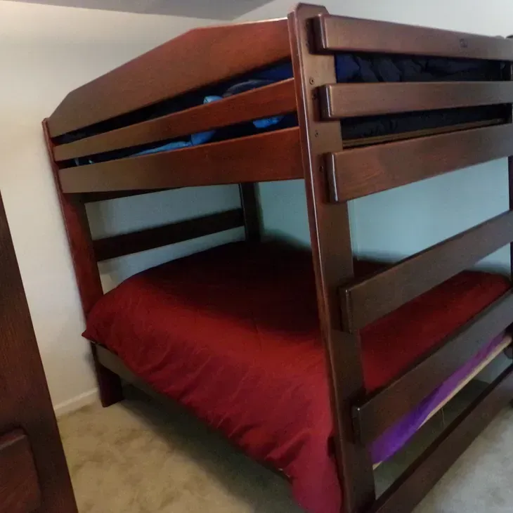 A wooden bunk bed with a red comforter in a bedroom