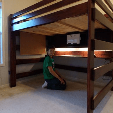 A boy in a green shirt is kneeling under a bunk bed