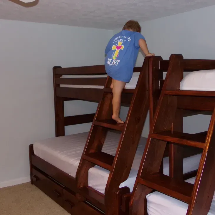 A child climbs a bunk bed with a shirt that says jesus on it