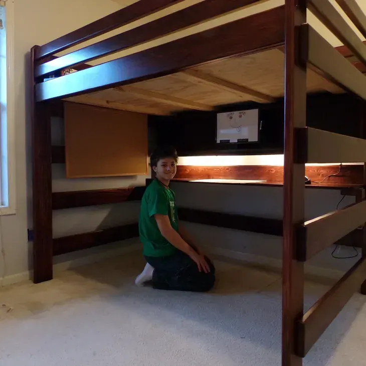 A boy in a green shirt is kneeling under a bunk bed