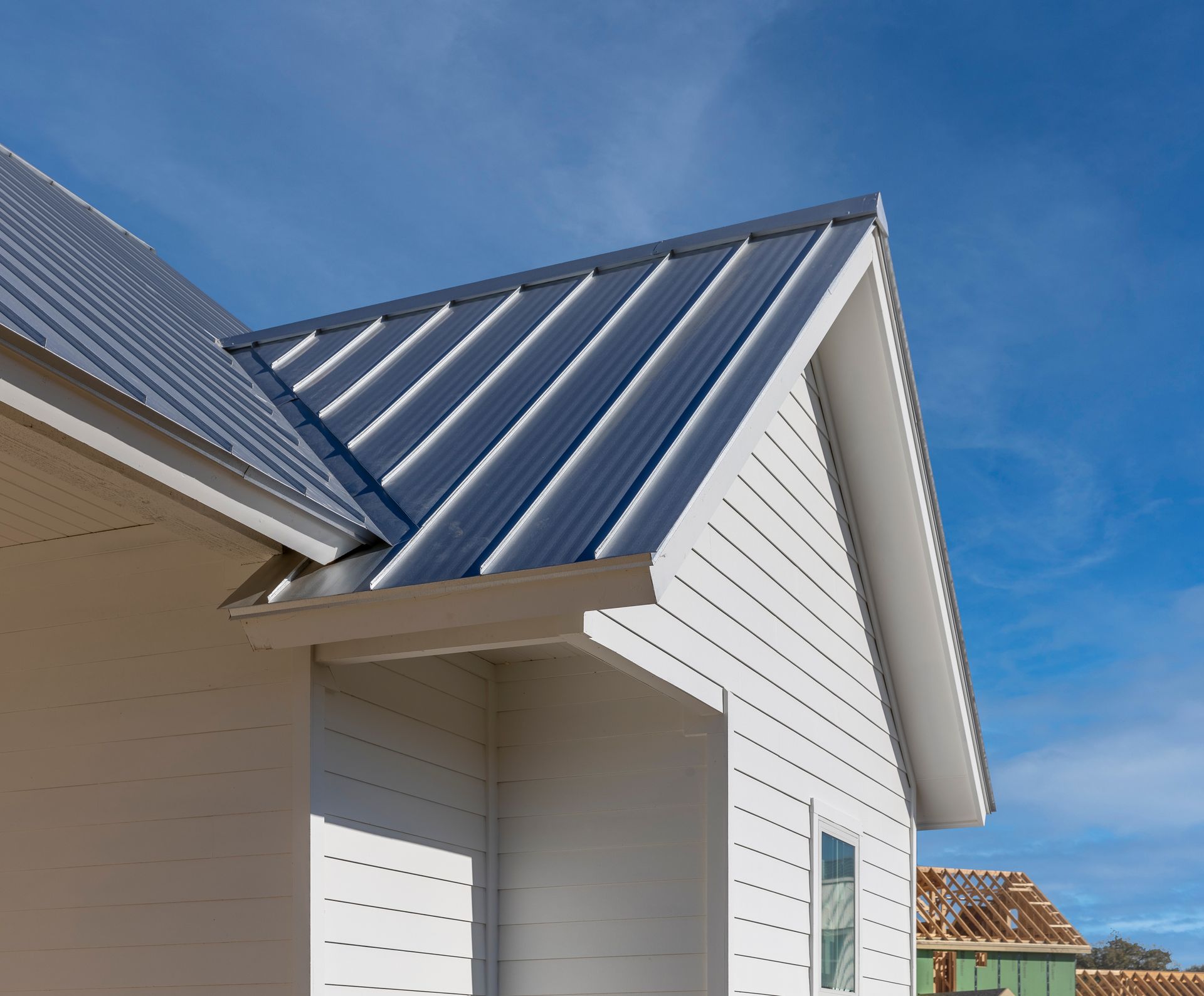 A white house with a metal roof and a blue sky in the background