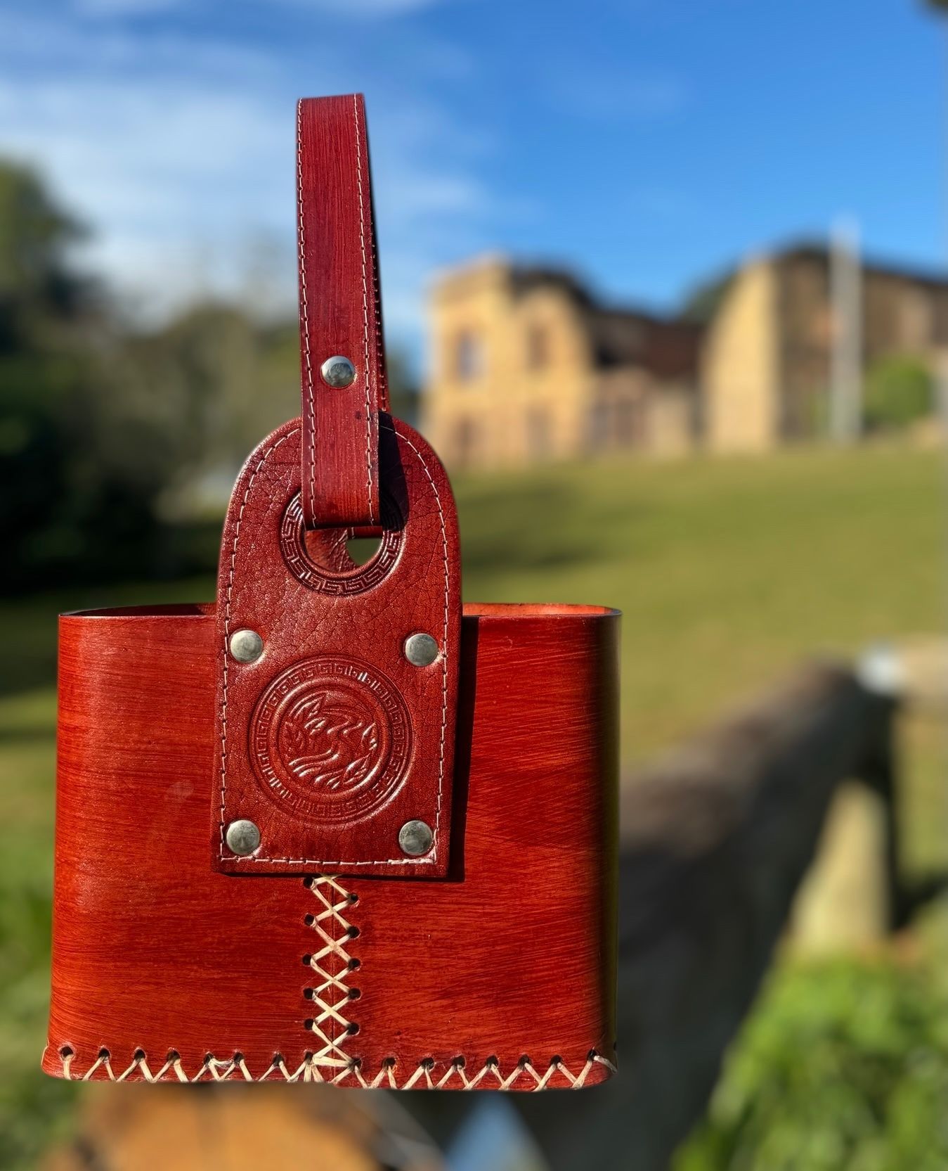 Un bolso de cuero marrón está sobre una valla de madera con una casa al fondo.