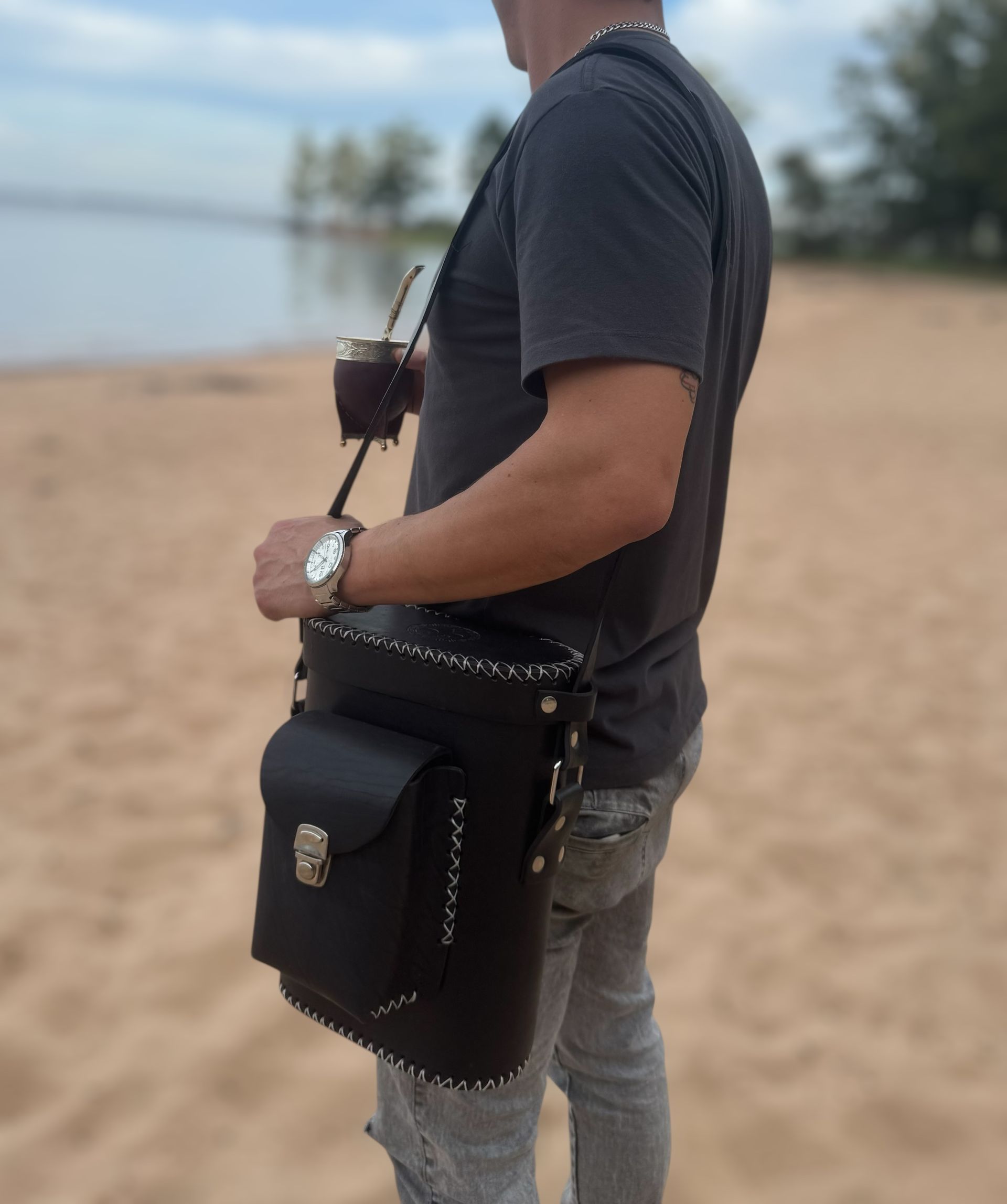 Un hombre parado en una playa sosteniendo una taza y una bolsa.