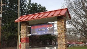 Sign for European Plus auto repair; red roof, stone pillars. | European Plus