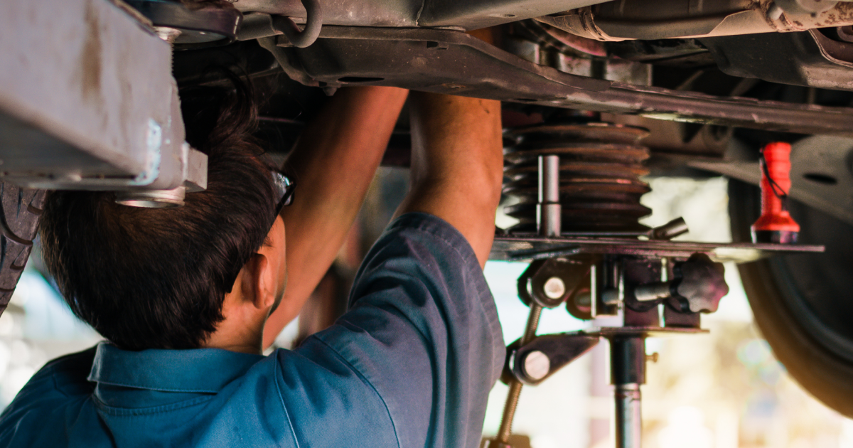 Mechanic working under a car, using a lift.  Blue shirt, dark hair. | European Plus