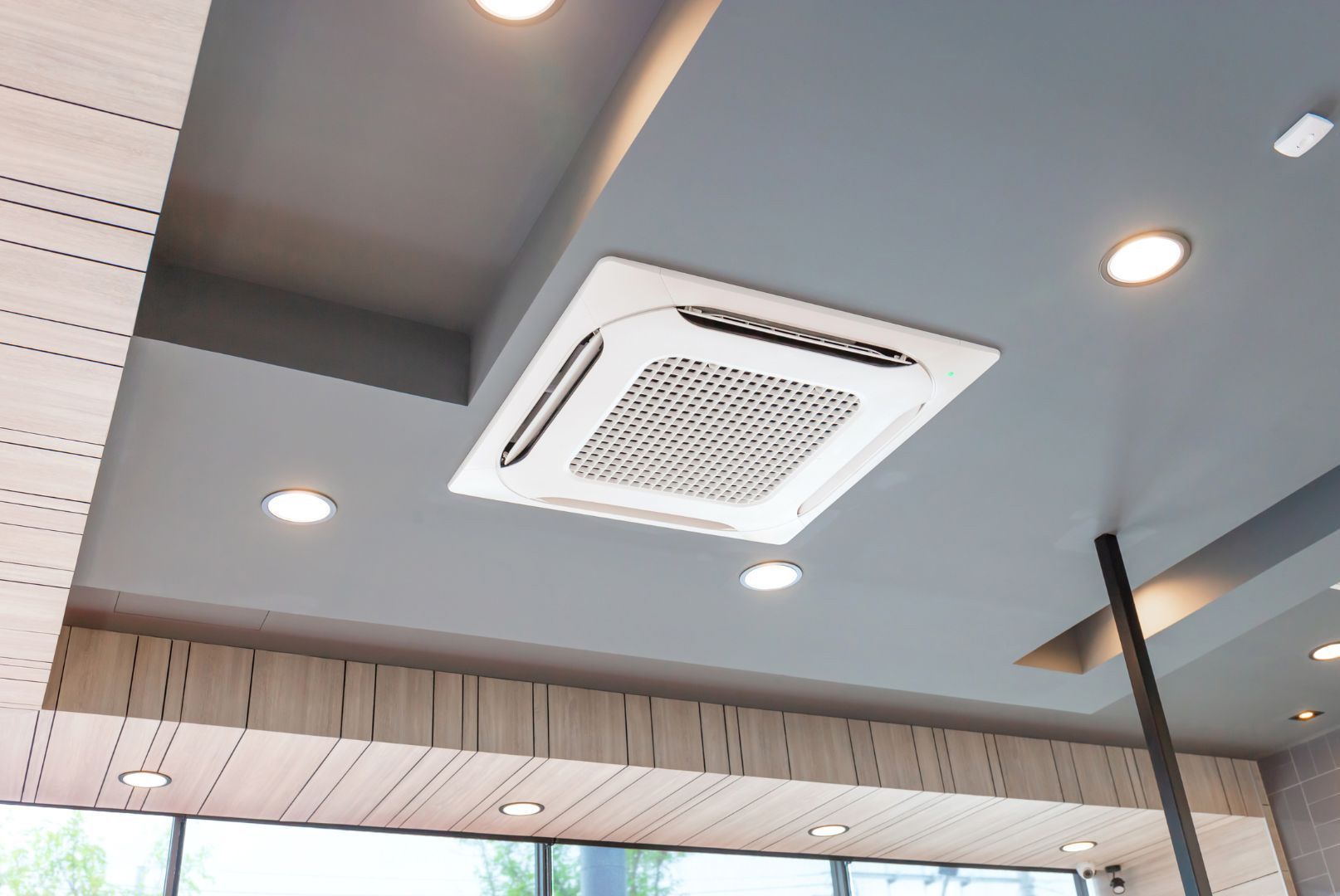 A square air conditioner is hanging from the ceiling of a room.