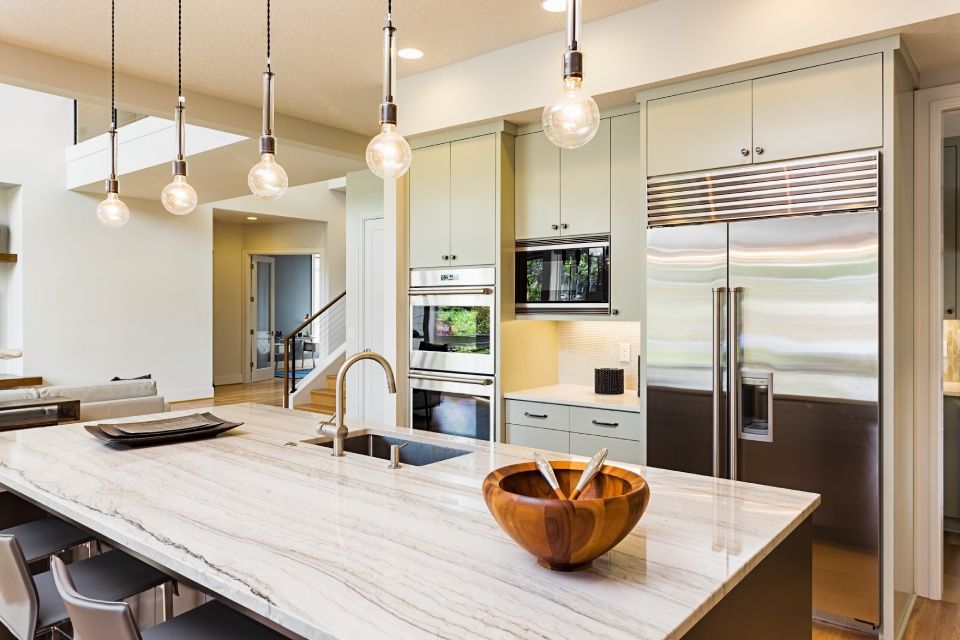 Kitchen Interior with Sink, Cabinets, Stainless Steel Refrigerator, Pendant Lights, and Hardwood Floors in New Luxury Home