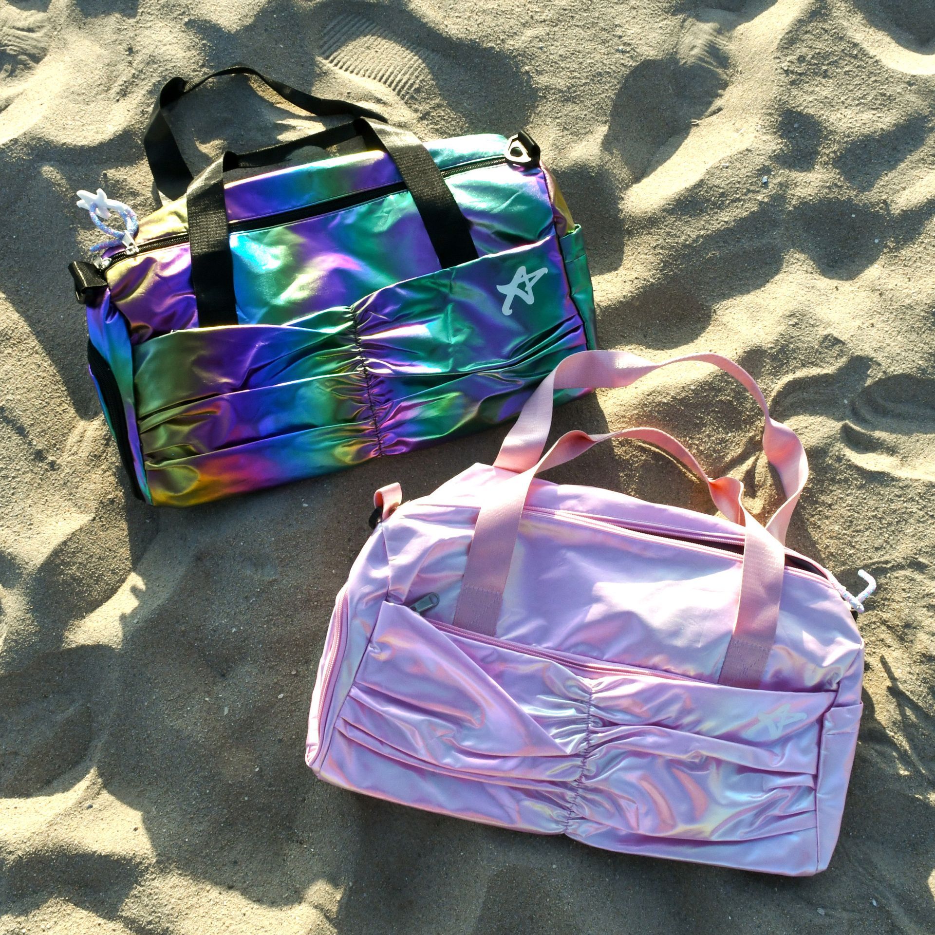 A purple and a rainbow duffel bag are on the sand