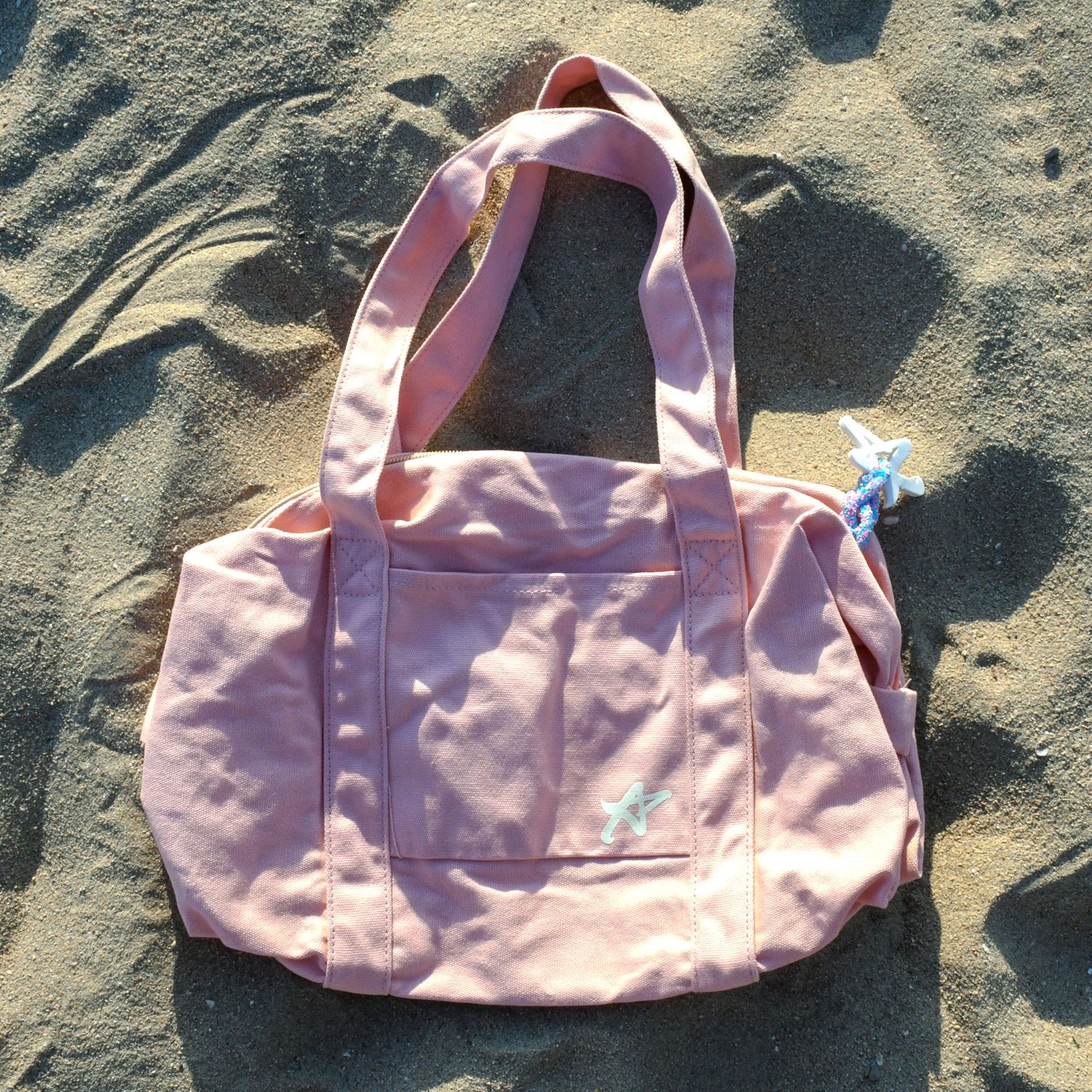 A pink tote bag is laying on a sandy beach