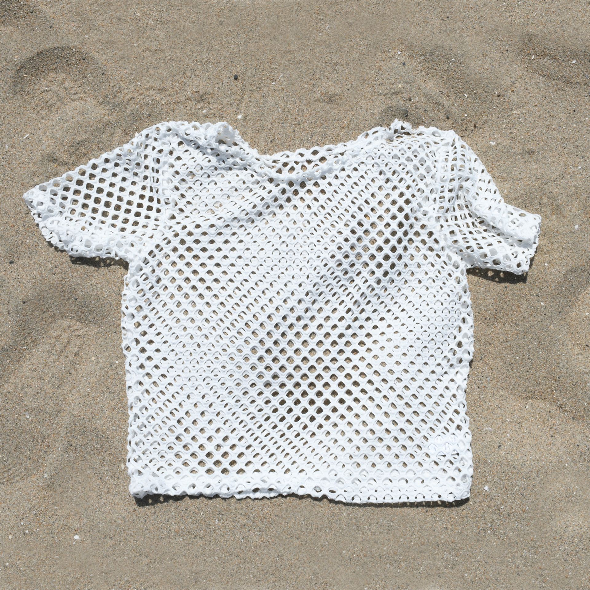 A white mesh top is laying on the sand