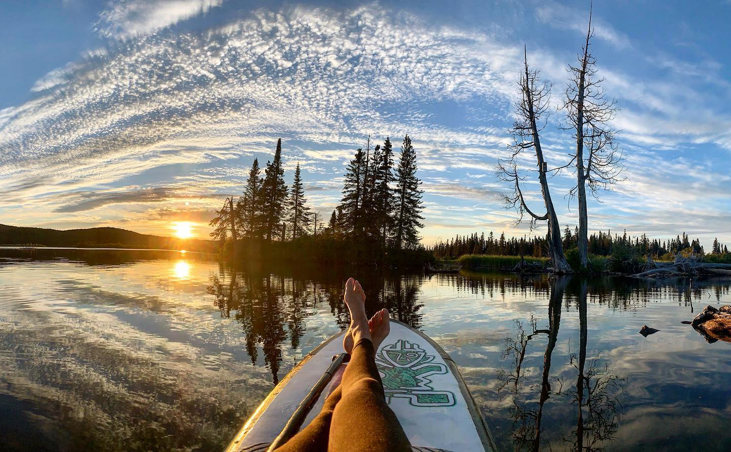 Legs relaxing on paddleboard pointing towards sunset on lake