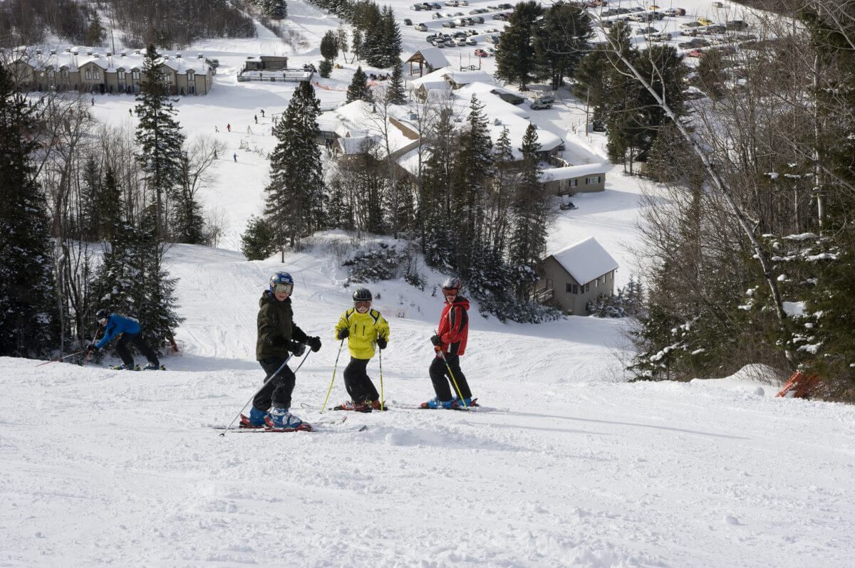 3 downhill skiers posing on hill with resort below