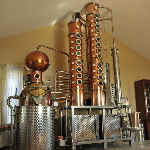 Large distillery machine made of copper, brass, and stainless steel.