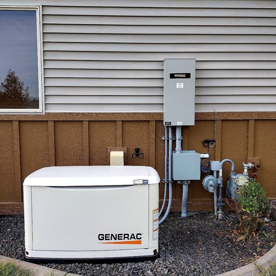 White Generac standby generator beside gray electrical panels and utility meters on a house exterior.