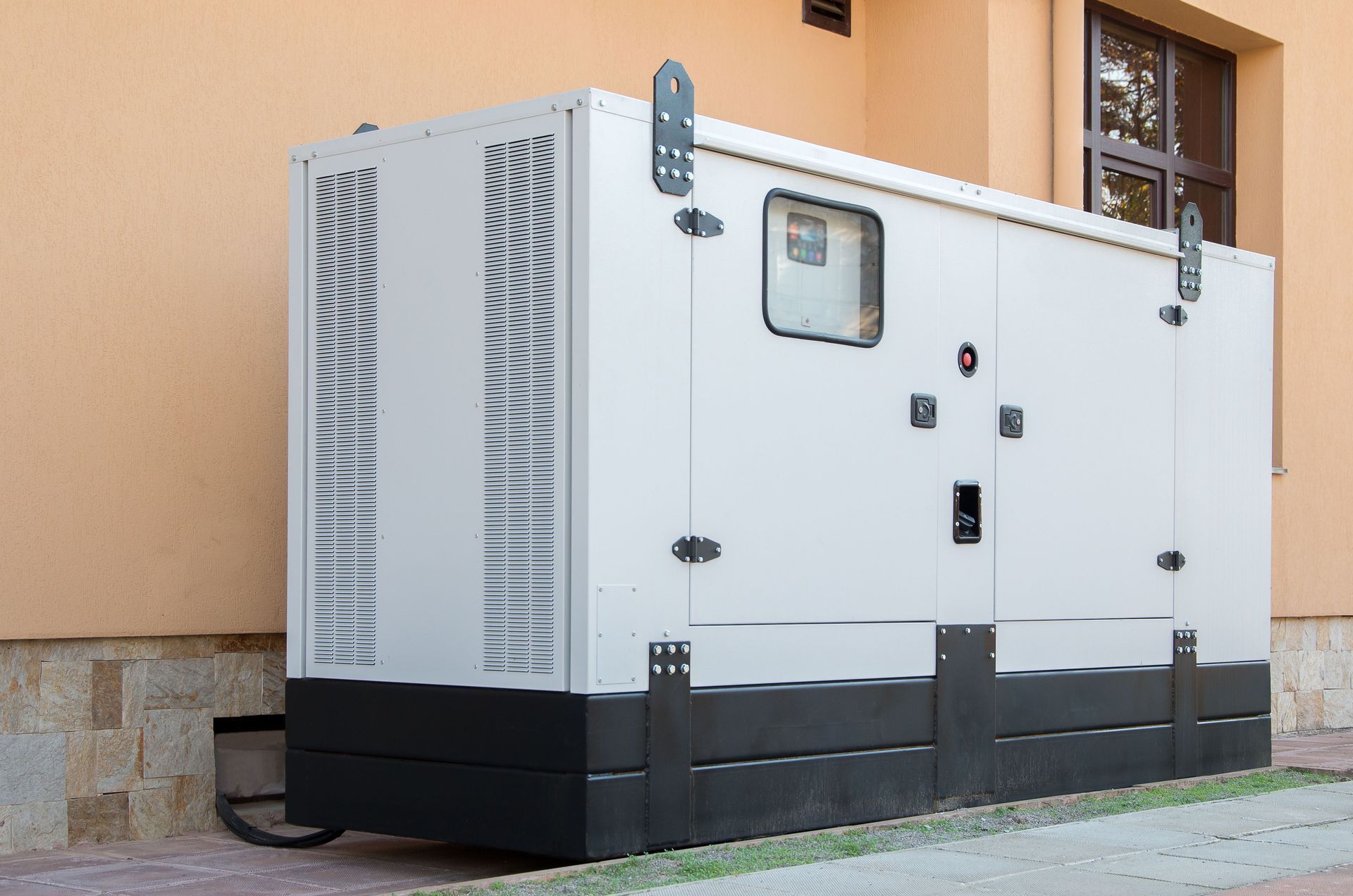Large white outdoor generator unit beside a building, with black base and vents on the side.