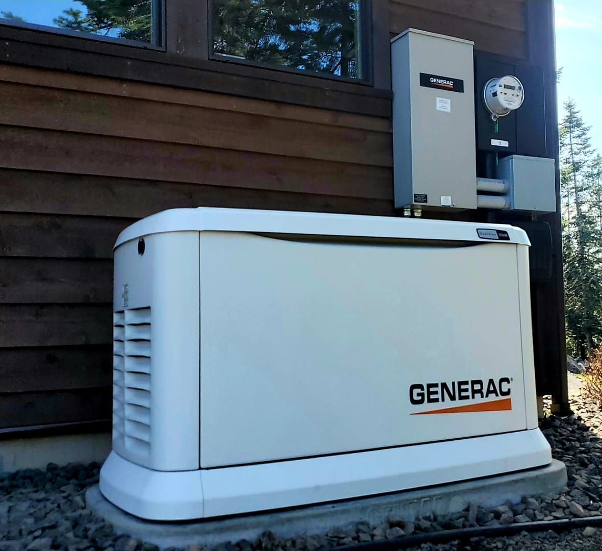 White Generac standby generator beside a house exterior wall with electrical panel above it.