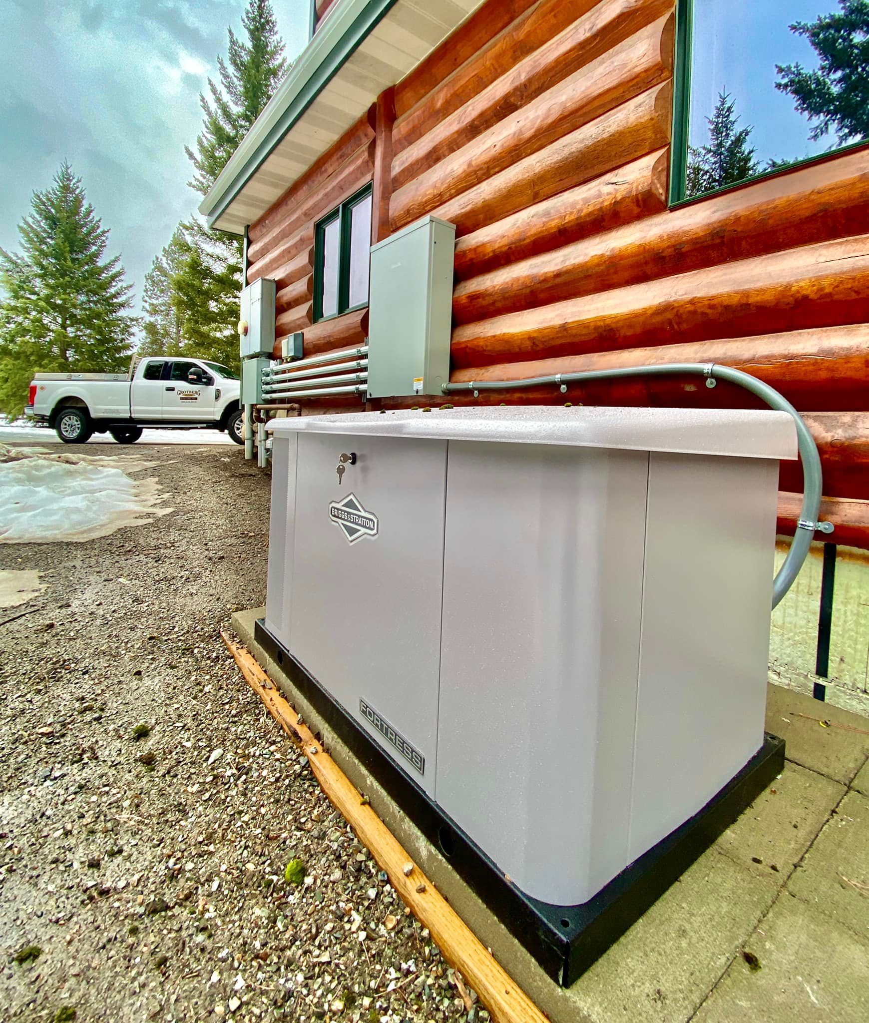 White hot tub beside a log cabin, with a white pickup truck parked on a gravel driveway.