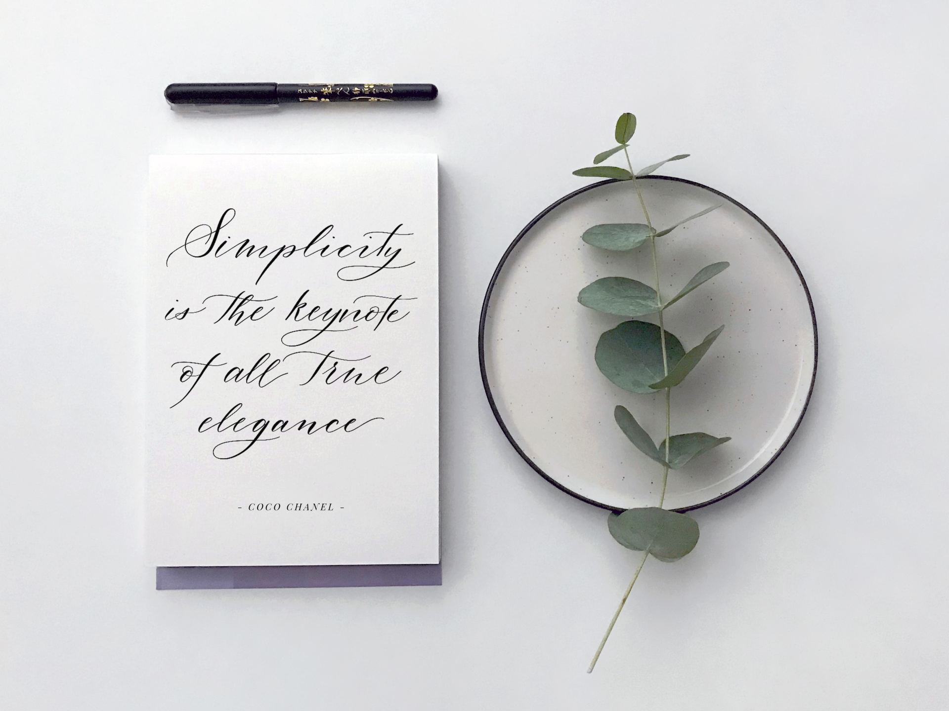 Calligraphy on a notebook beside a eucalyptus branch