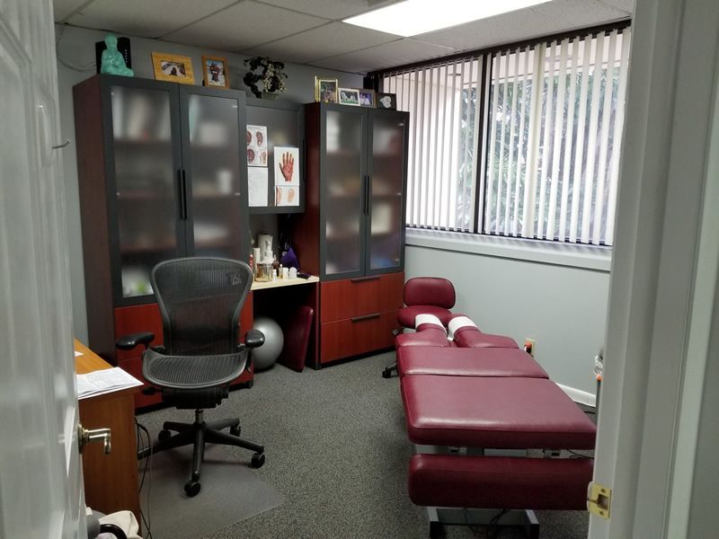A chiropractor's office with a treatment table, office cabinets, and a desk chair.