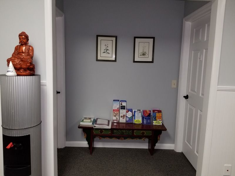 Buddha statue on water cooler, table with brochures between two doors, grey walls, and framed artwork.