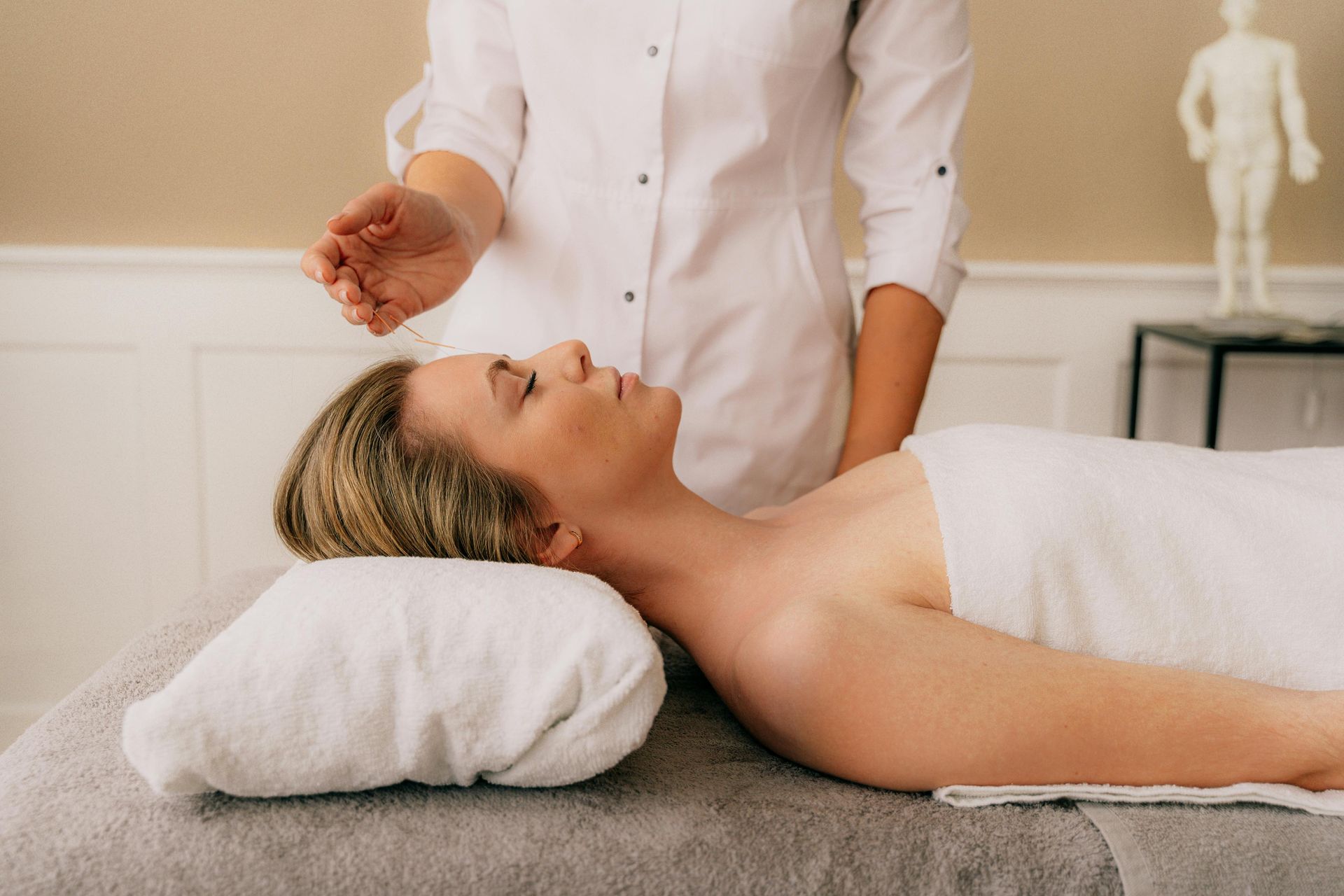 A person lying on a massage table with closed eyes while a practitioner holds a hand above their forehead.