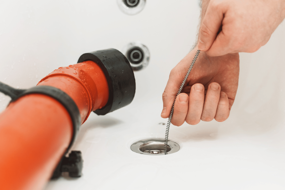 A person is cleaning a drain in a bathtub with a plunger.