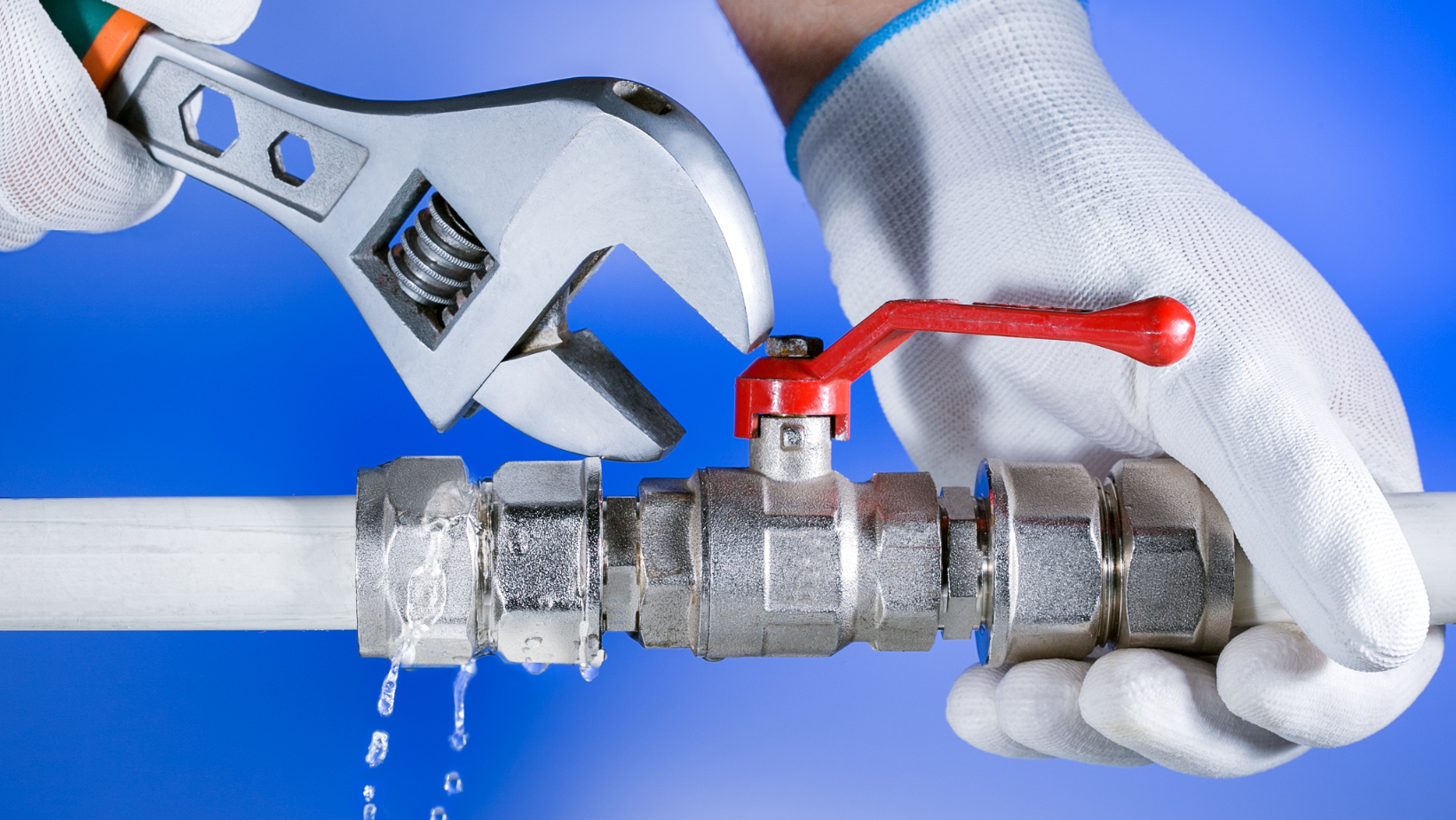 A plumber is fixing a leaking pipe with a wrench.