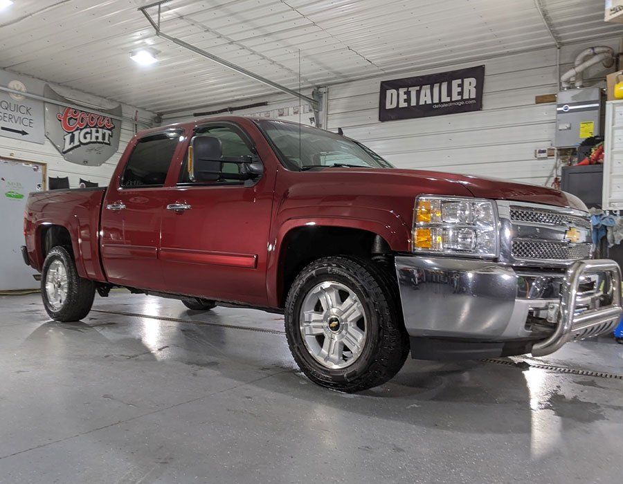 A red truck is parked in a garage next to a sign that says detailer.