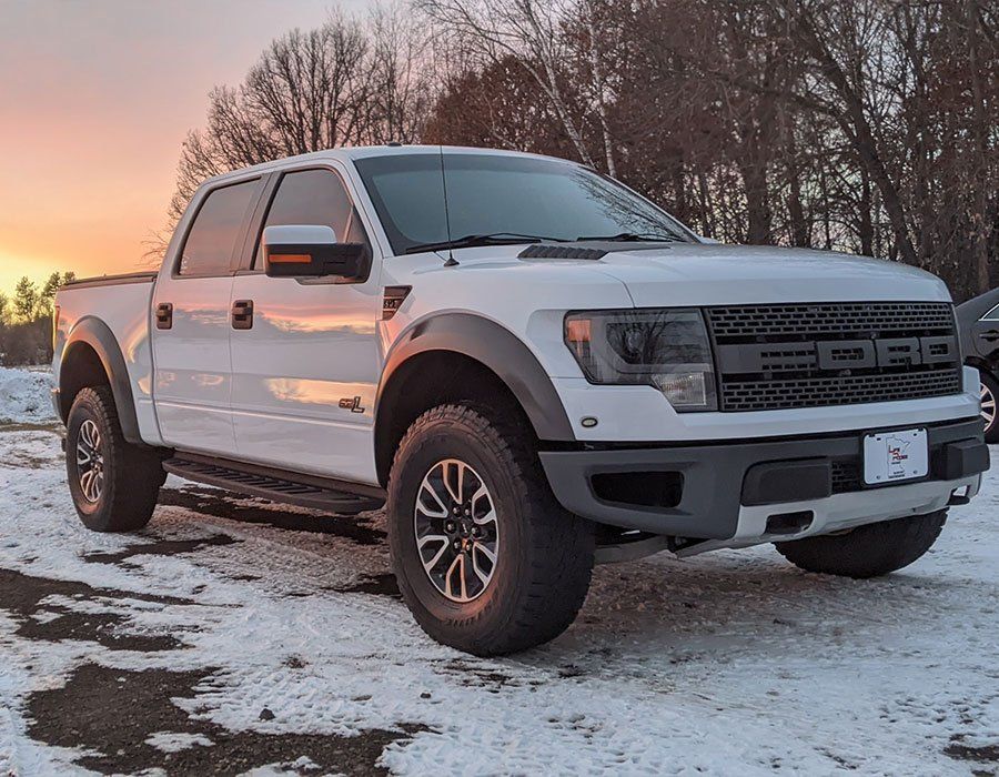 A white ford raptor pickup truck is parked in the snow.