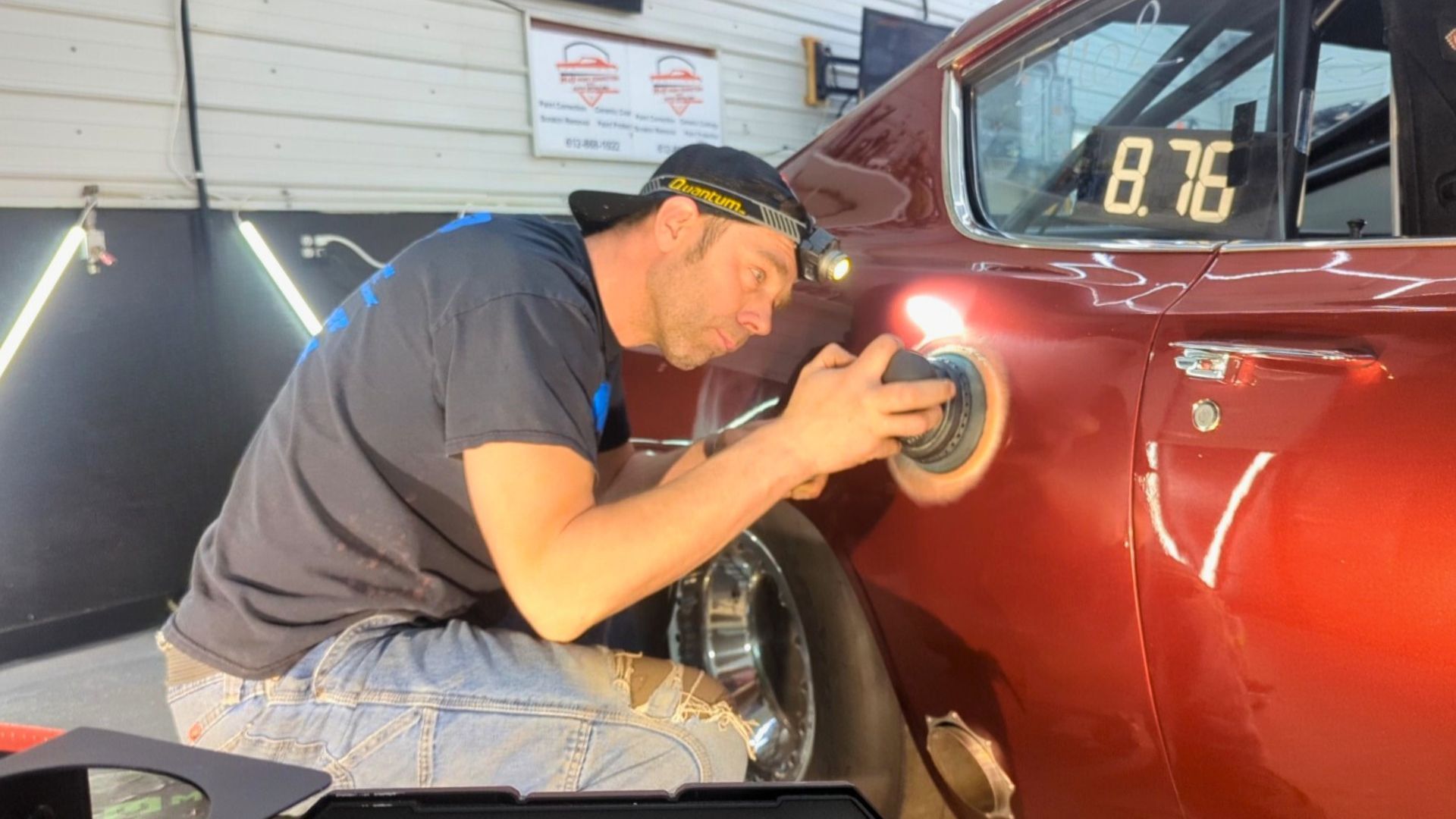 Man polishing a red classic car with a buffer in a garage.