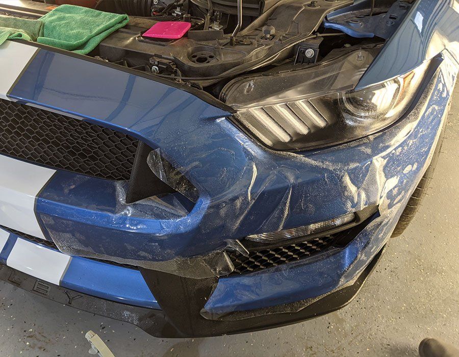 A blue mustang is wrapped in plastic and sitting in a garage.
