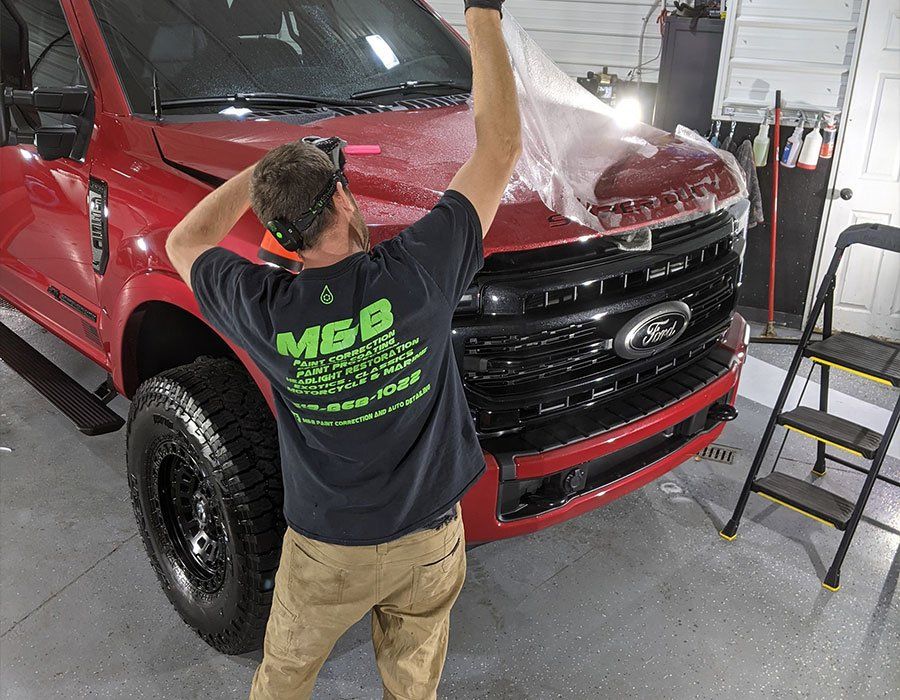 A man is wrapping a red truck with plastic wrap.