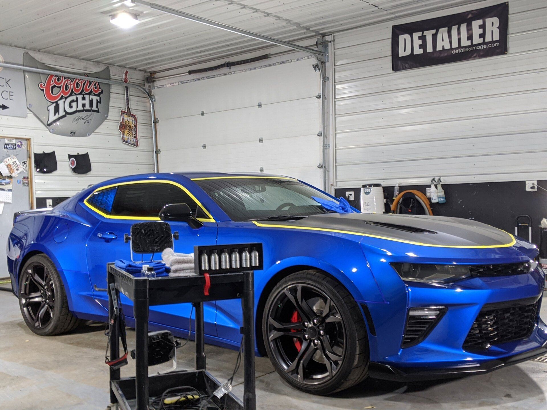 A blue car is parked in a garage next to a detailer sign.