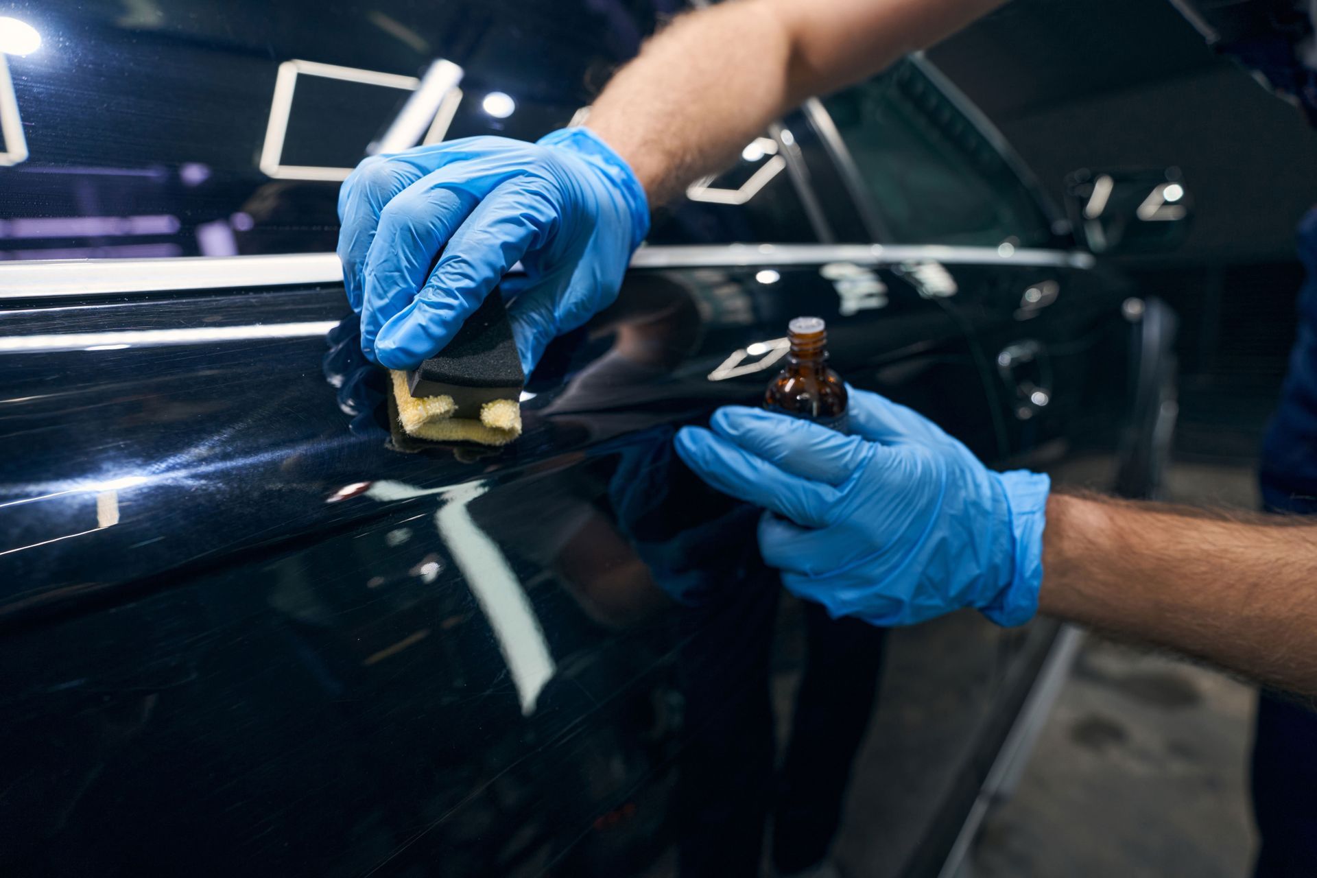 A person wearing blue gloves is polishing a car door with a sponge.