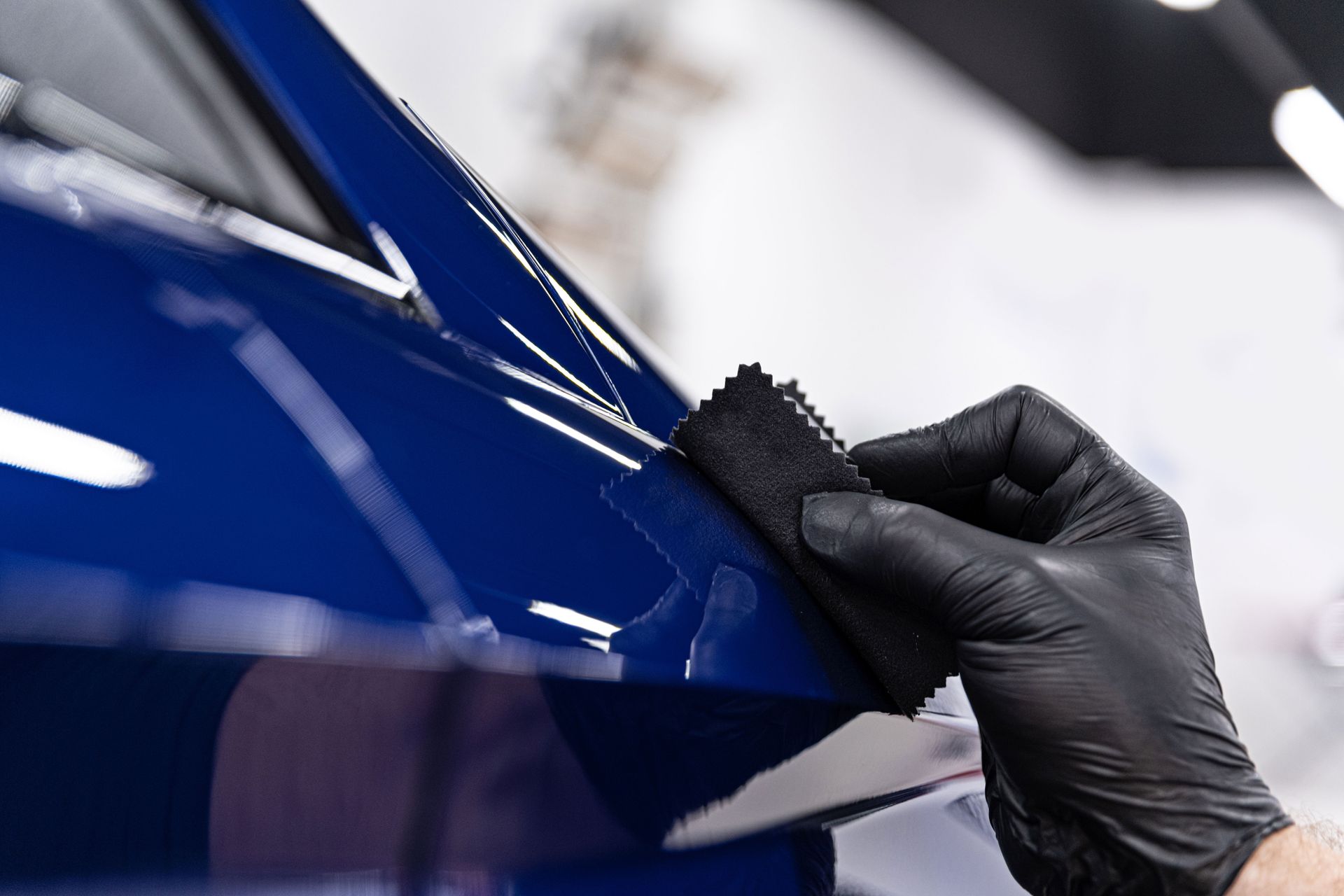 A person wearing black gloves is polishing a blue car with a sponge.