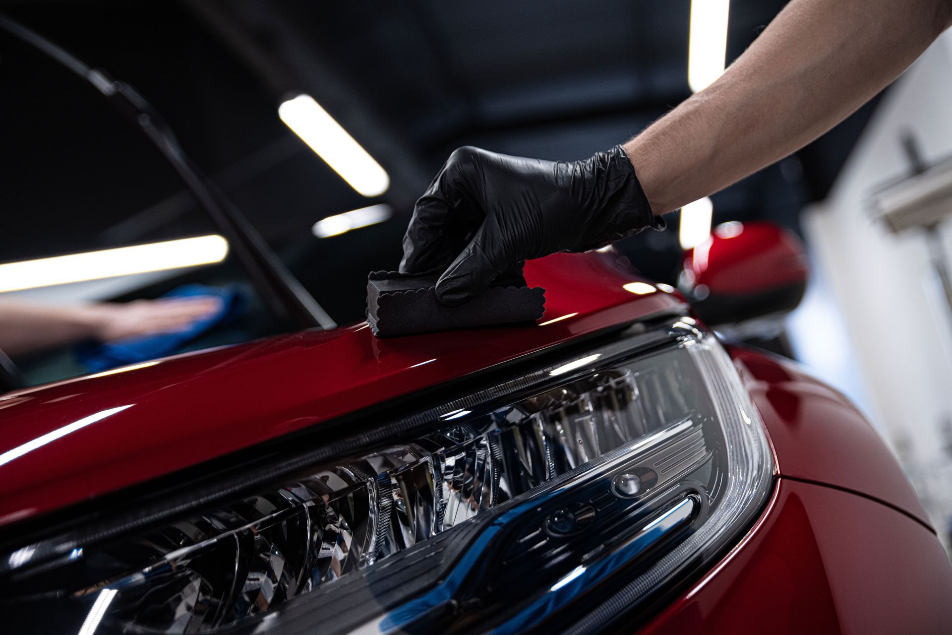 A person is polishing the headlight of a red car.