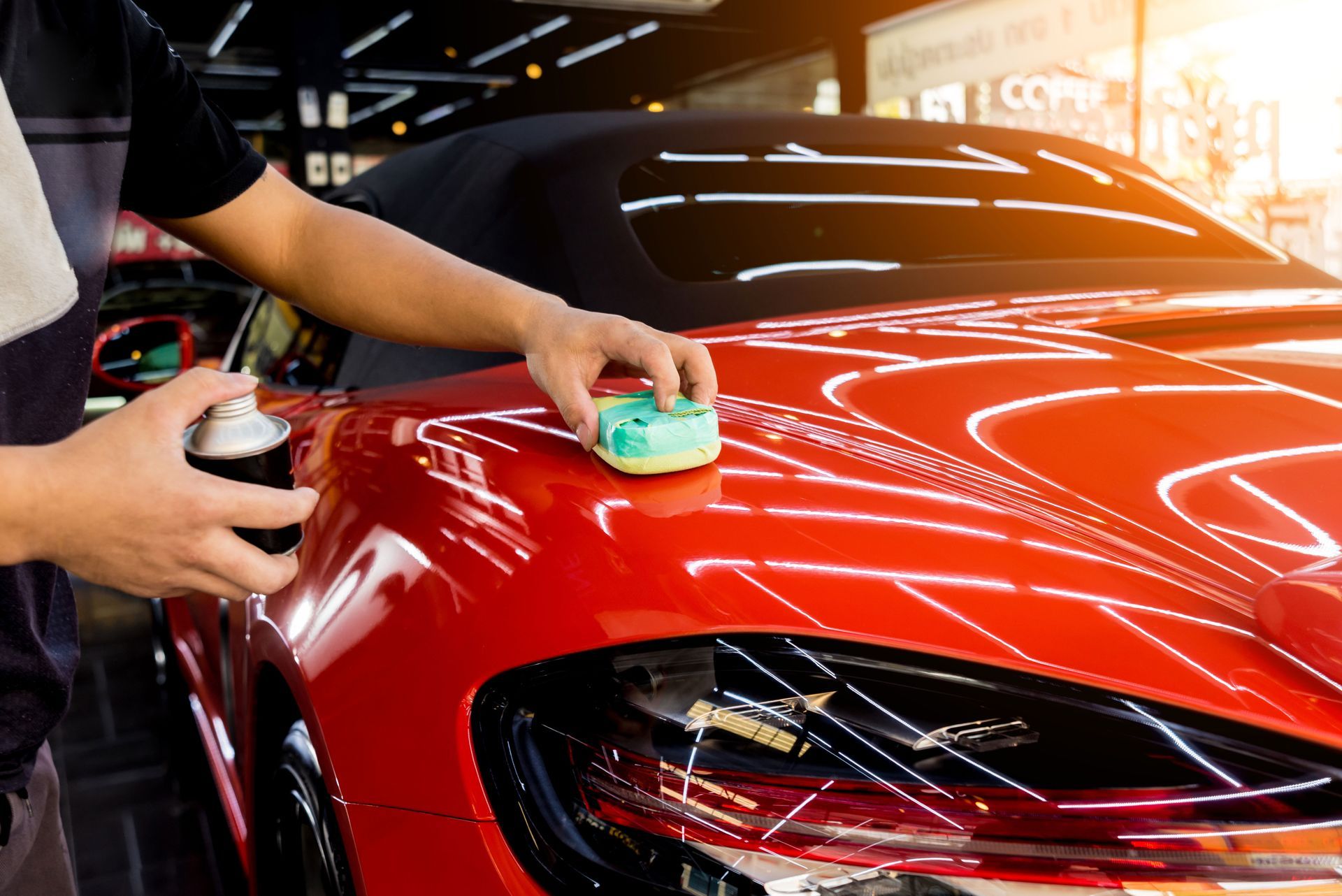 A man is polishing a red car with a sponge.