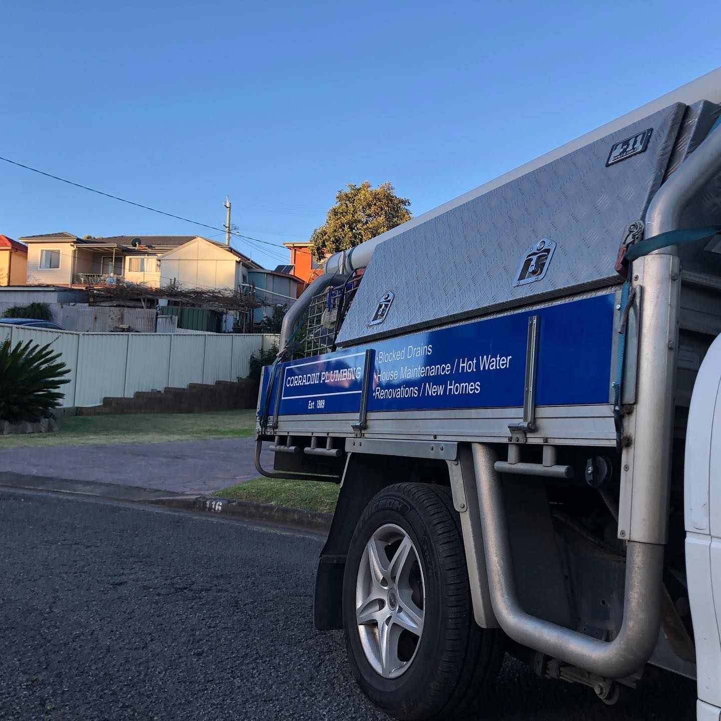 White utility truck parked on a street with houses in the background on a sunny day.