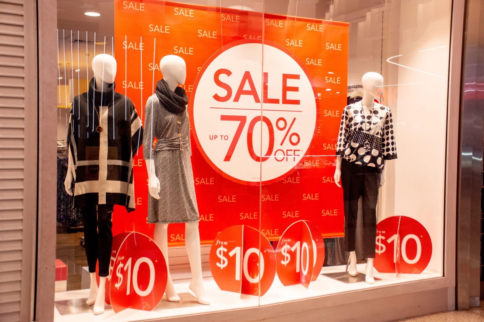 Clothing store window display with mannequins showcasing sale items, including a 70% off sale.