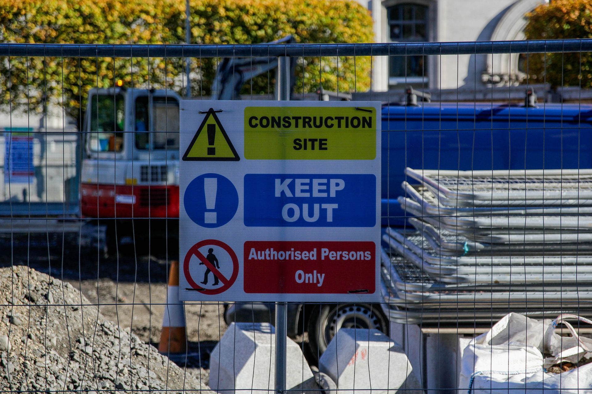 Construction site sign: Warning, keep out. Authorized persons only. Fenced area with machinery in background. Construction site sign: Warning, keep out. Authorized persons only. Fenced area with machinery in background.