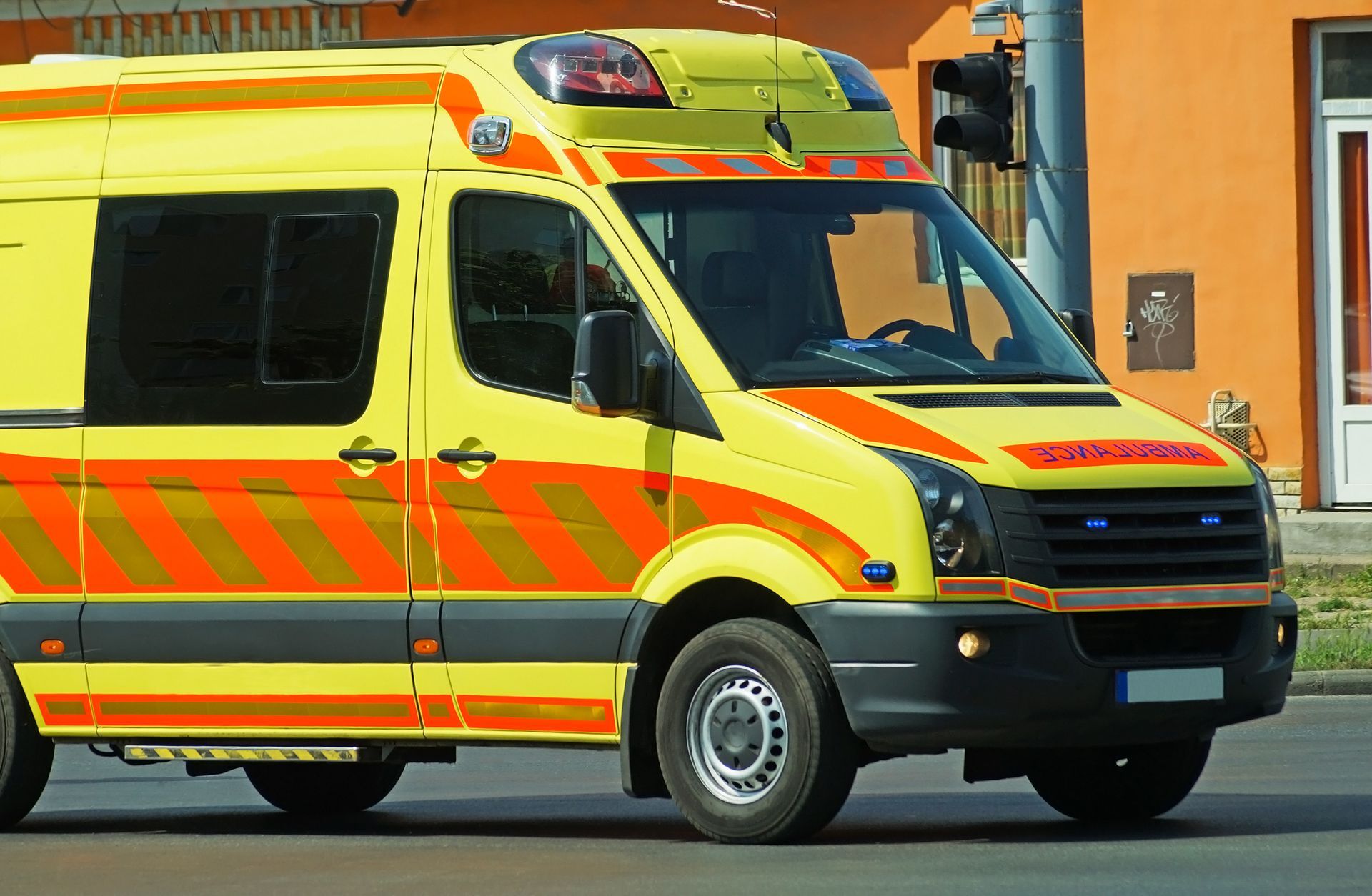 Yellow and orange ambulance on a street in front of an orange building. Yellow and orange ambulance on a street in front of an orange building.