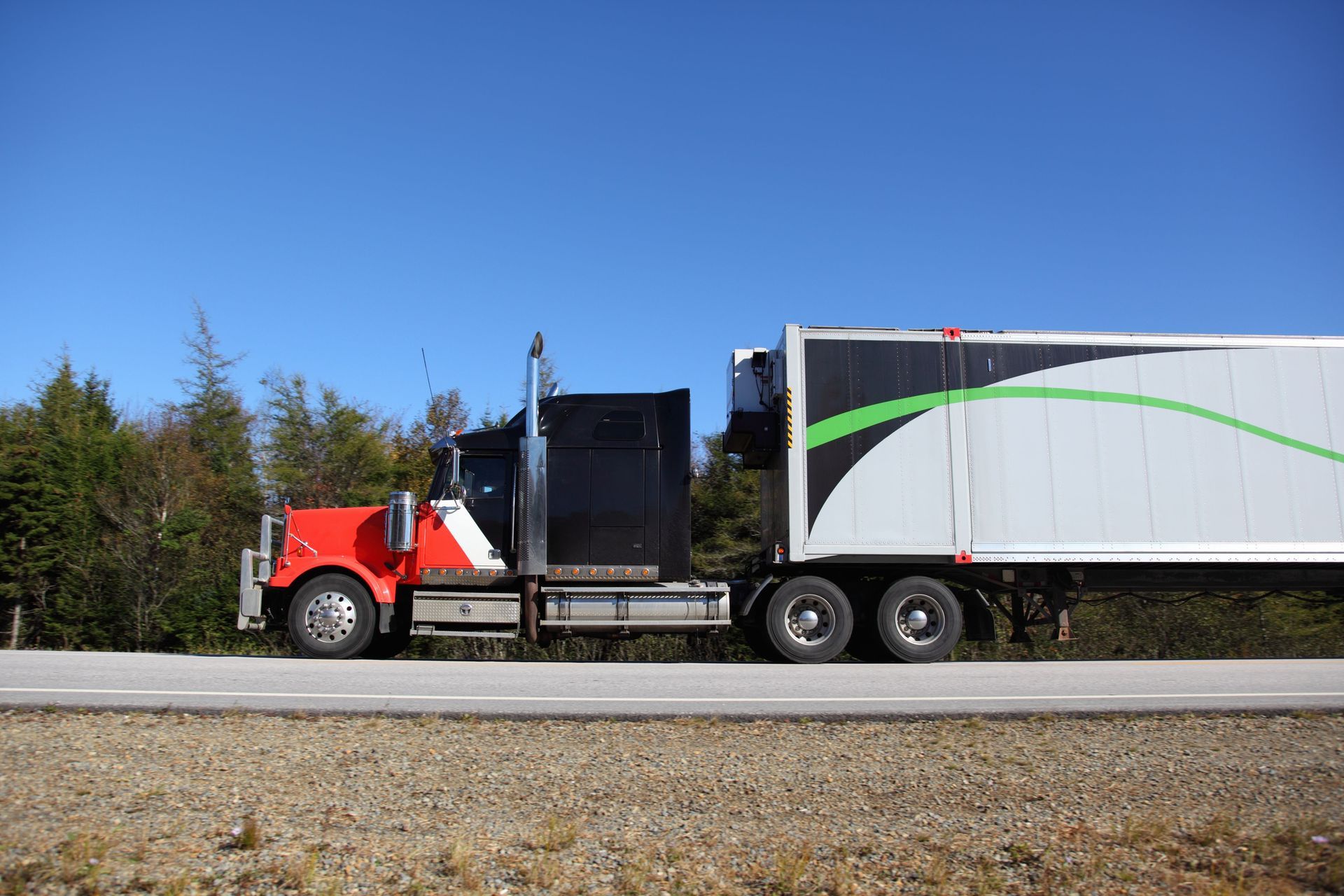 Red and black semi-truck on asphalt road, gray trailer with green accent, blue sky backdrop. Red and black semi-truck on asphalt road, gray trailer with green accent, blue sky backdrop.