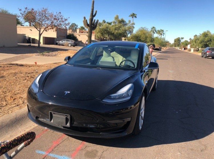 A black tesla model 3 is parked on the side of the road.