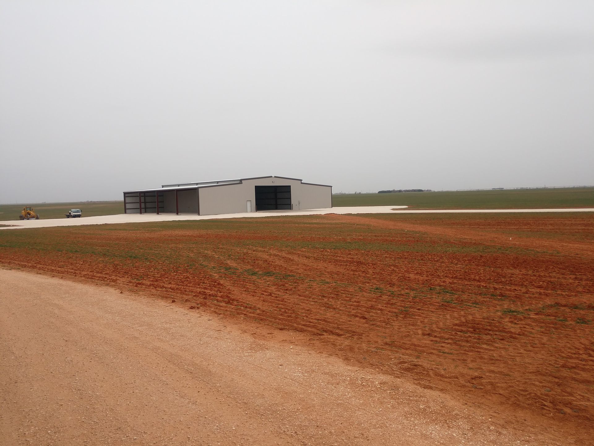 A dirt road leads to a building in the middle of a field