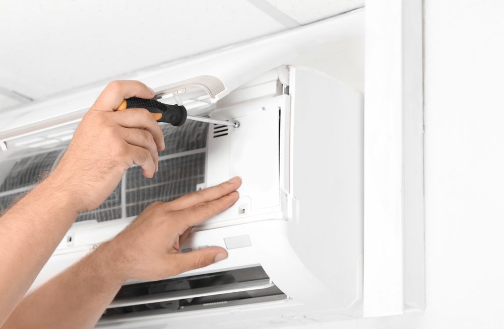 Person Using Screwdriver to Repair White Air Conditioner — Craig Stewart Electrical in East Wagga Wagga, NSW