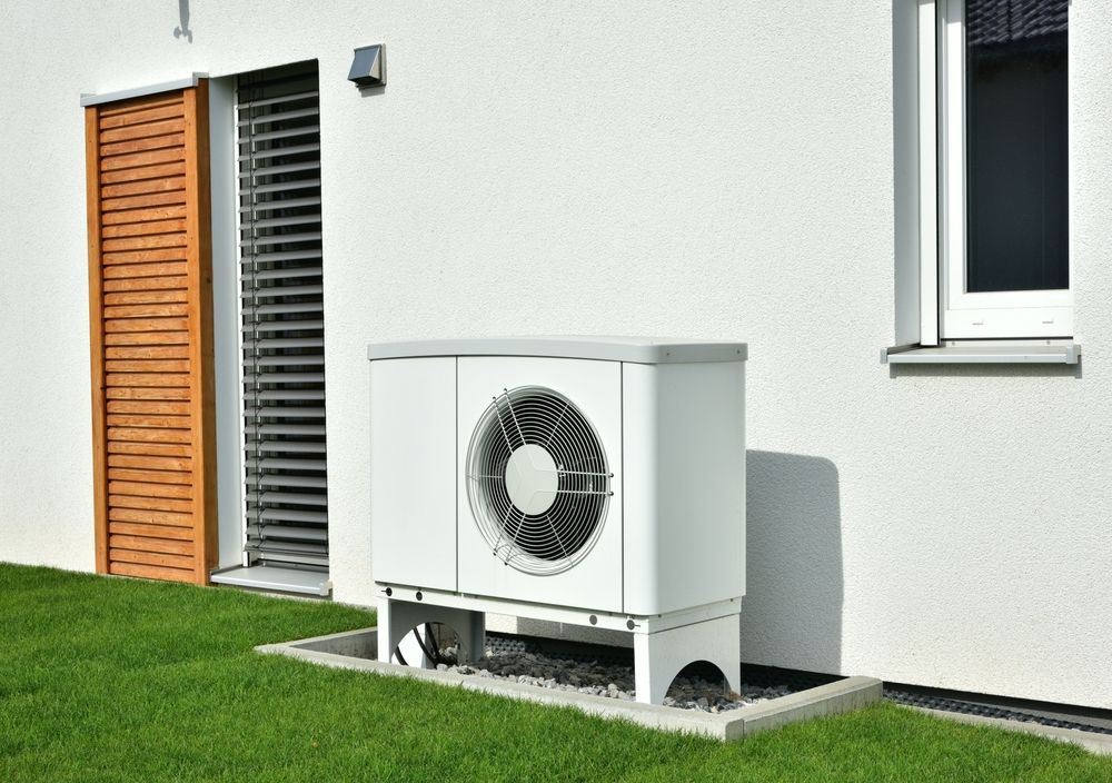 White Heat Pump Next to a House With a Wooden Shutter and Green Lawn — Craig Stewart Electrical in East Wagga Wagga, NSW
