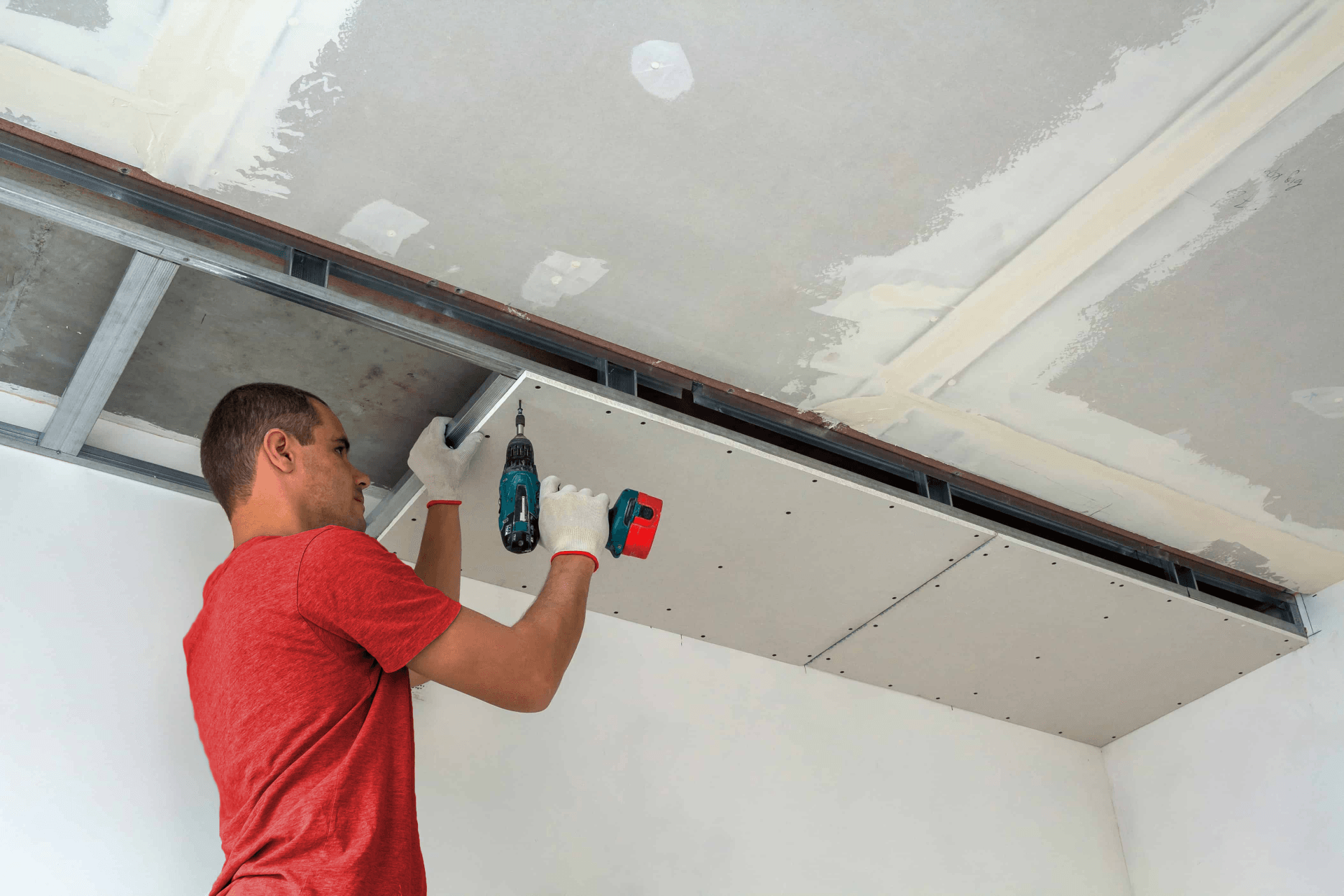 A man is installing a drywall ceiling in a room.